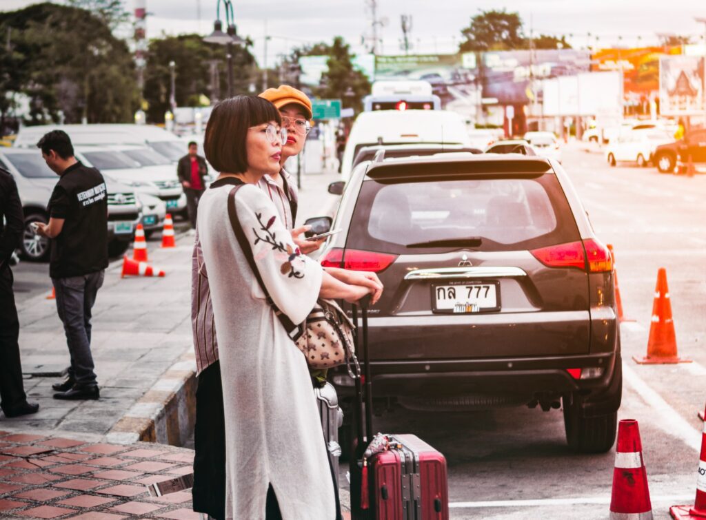 Women standing with suitcases near a parked car