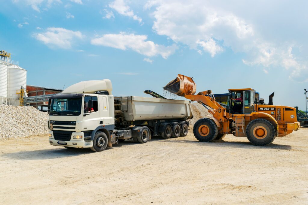 A brown loader beside a white cargo truck signifying movers that you can hire after you've found a real estate agent.