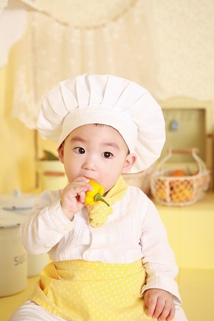 A child dressed up as a chef holding a pepper