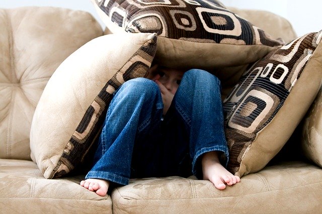 A boy hidden underneath cushions