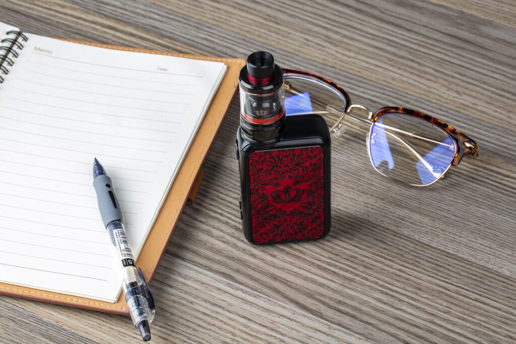 a vaping device in a table with glasses pen and a notebook