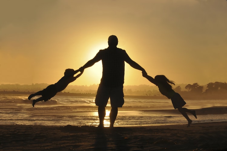 A dad playing on the beach with his kids during a gorgeous sunset.