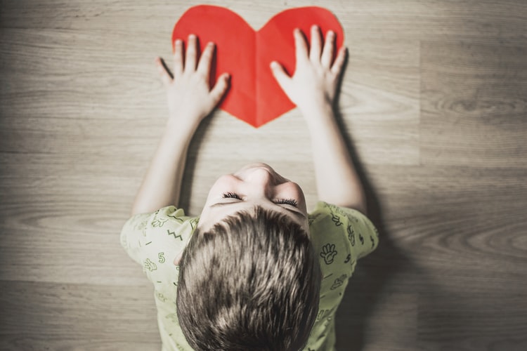 A cute little boy touching a paper heart.