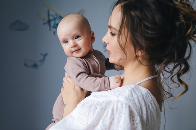 A woman carrying a baby who is wearing the brown onesie