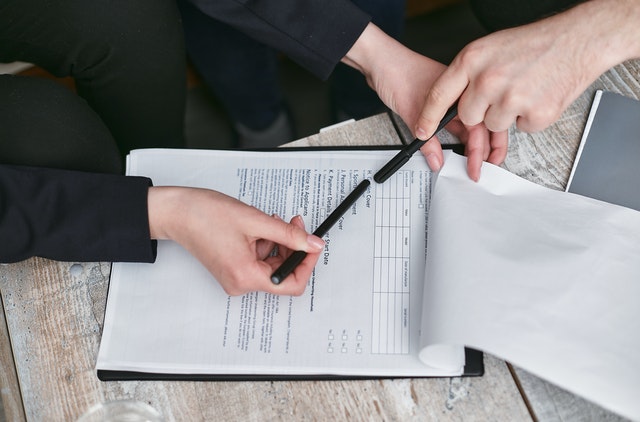 Two people holding black pens pointing at a paper form. 