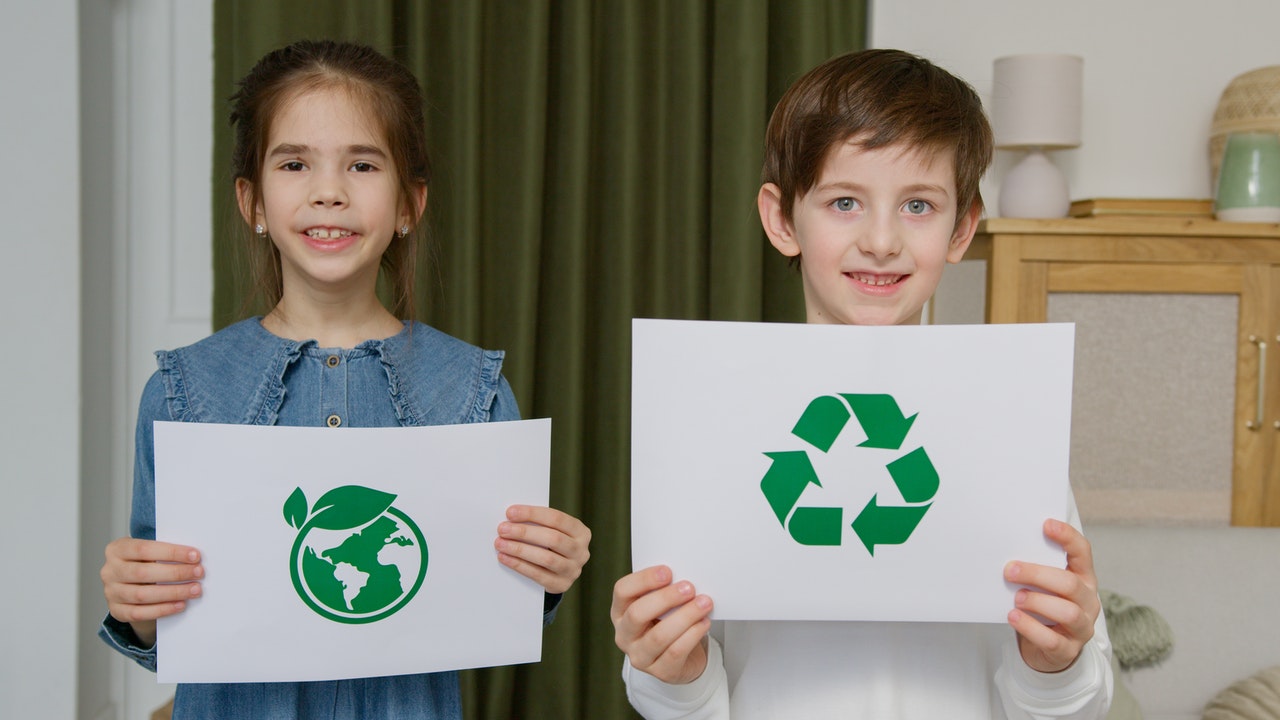 Two kids holding papers with recycling symbols