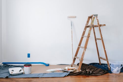 A freshly painted white wall, a ladder, a paintbrush, and paint material.