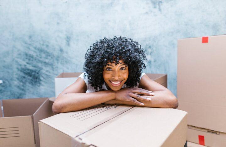 A woman with curly hair smiling while standing near packed boxes.