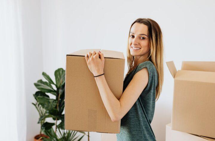 Cheerful woman carrying packed cardboard box