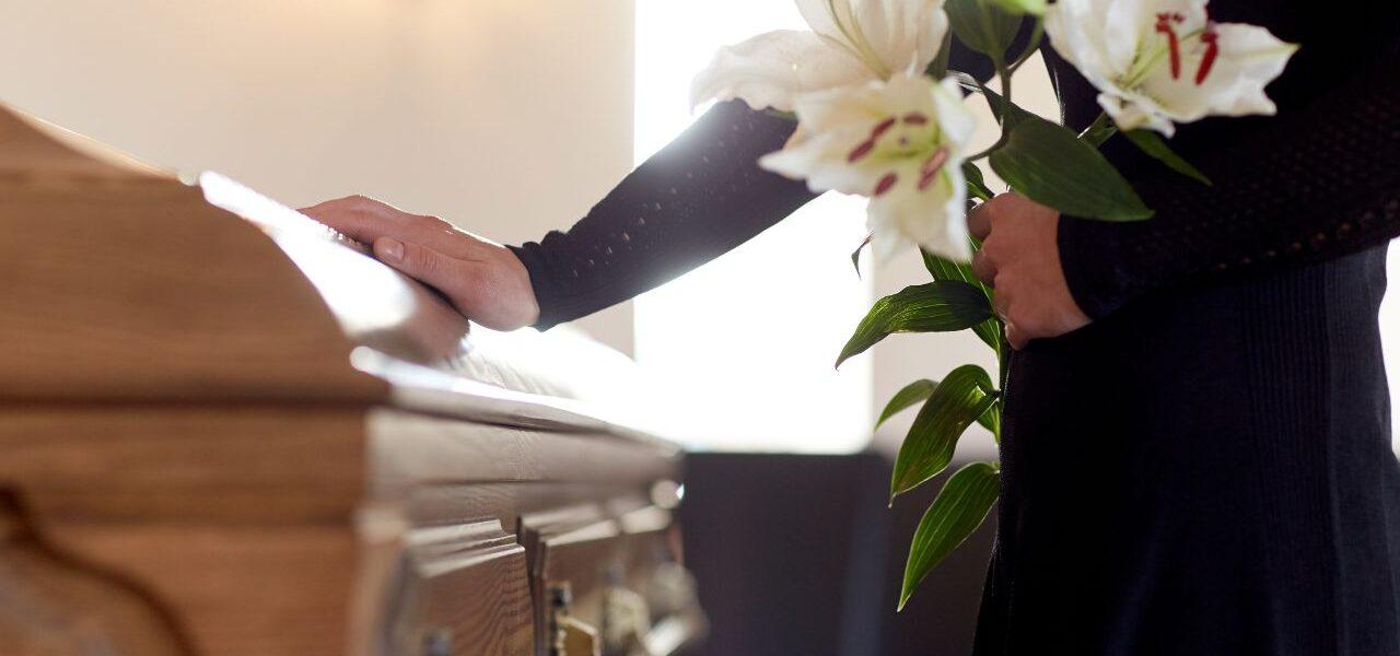 a person touching the coffin of a loved one with white flowers mourning