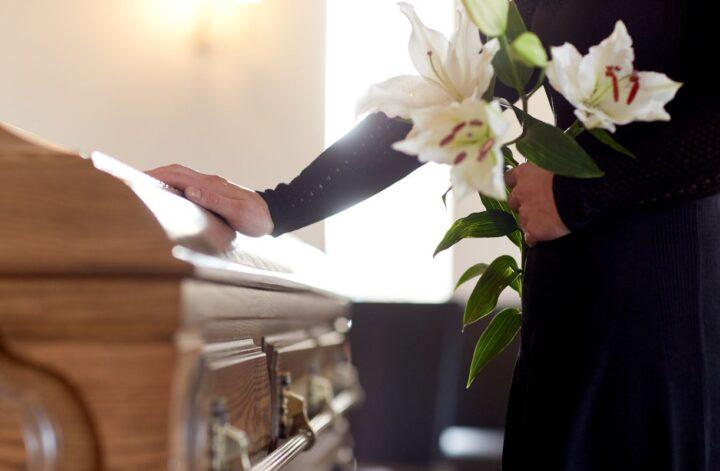 a person touching the coffin of a loved one with white flowers mourning