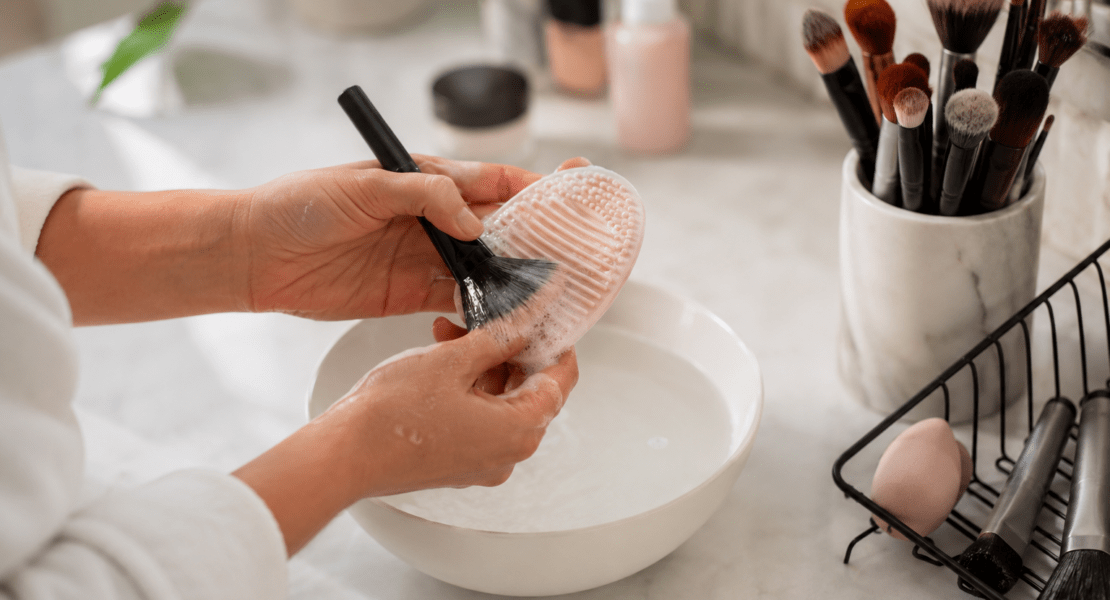 Person cleaning a makeup brush with a silicone brush cleaning mat to maintain makeup hygiene and healthy skin.