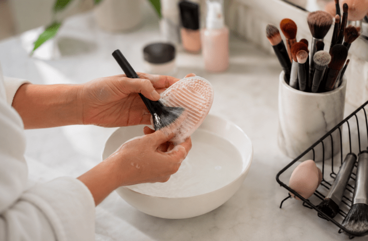 Person cleaning a makeup brush with a silicone brush cleaning mat to maintain makeup hygiene and healthy skin.