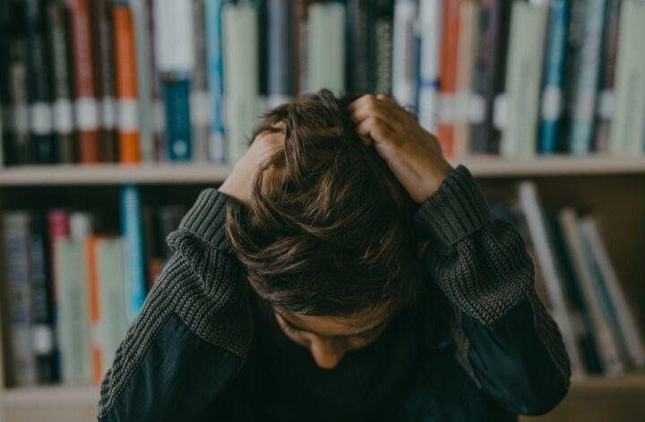 Teen sitting with head down and hands in hair in a library, illustrating signs of anxiety that parents may overlook.
