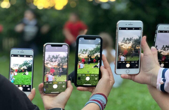 Several people using smartphones to photograph a group outdoors, illustrating teen phone use and screen time habits.