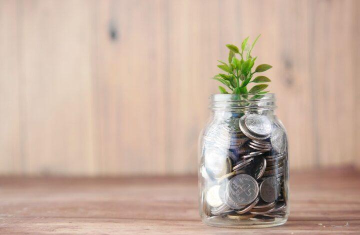 Glass jar filled with coins and a growing plant representing tax-efficient investing through ISAs and retirement accounts.