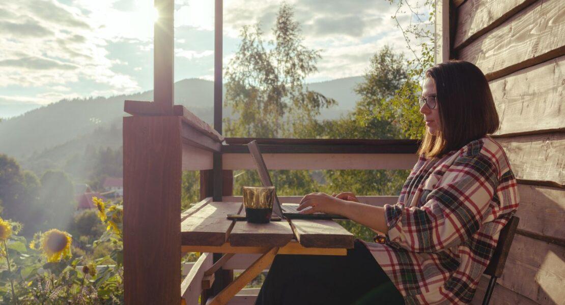 Woman working remotely on a laptop from a scenic cabin balcony