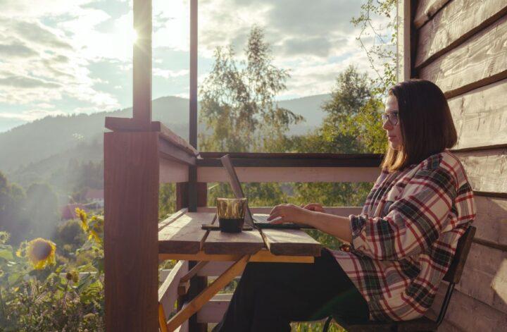 Woman working remotely on a laptop from a scenic cabin balcony