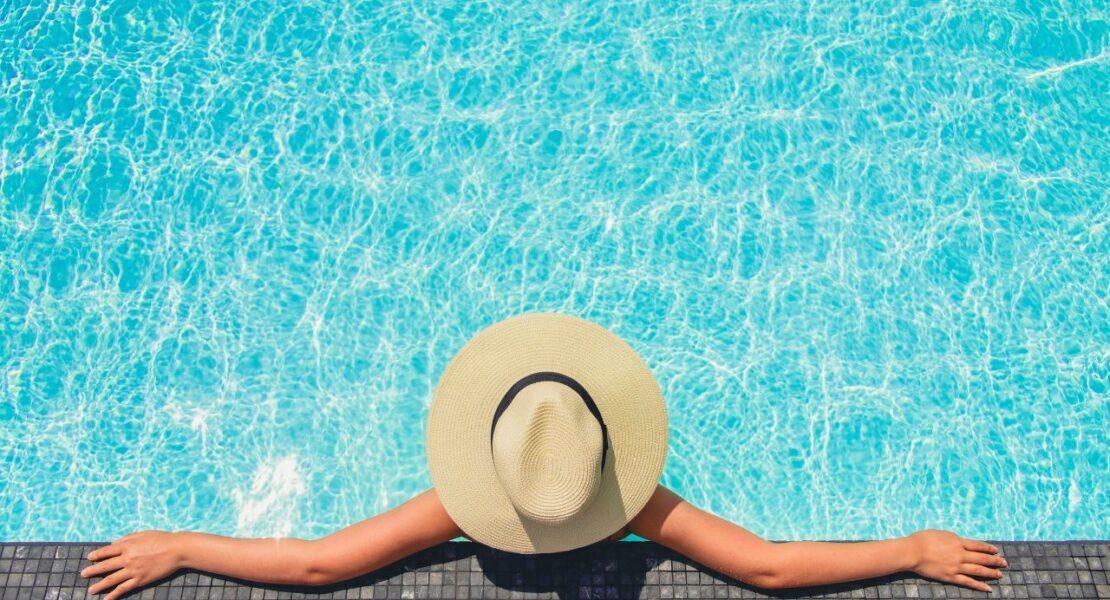 Person relaxing at the edge of a swimming pool during peak swimming season