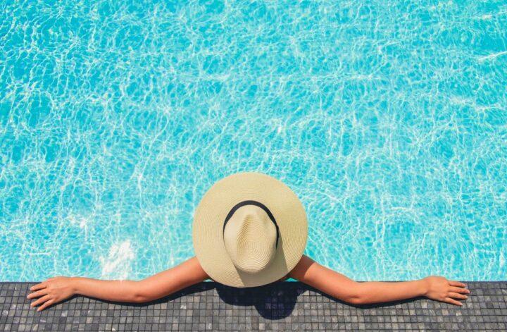Person relaxing at the edge of a swimming pool during peak swimming season