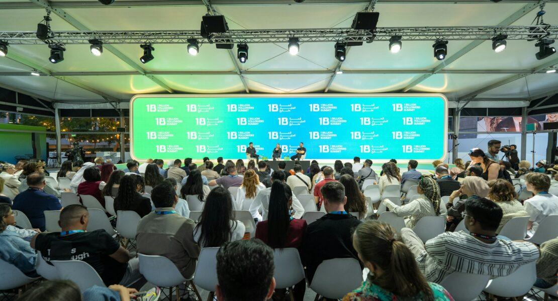Audience attending a conference with branded event signage and stage presentation for event promotion.