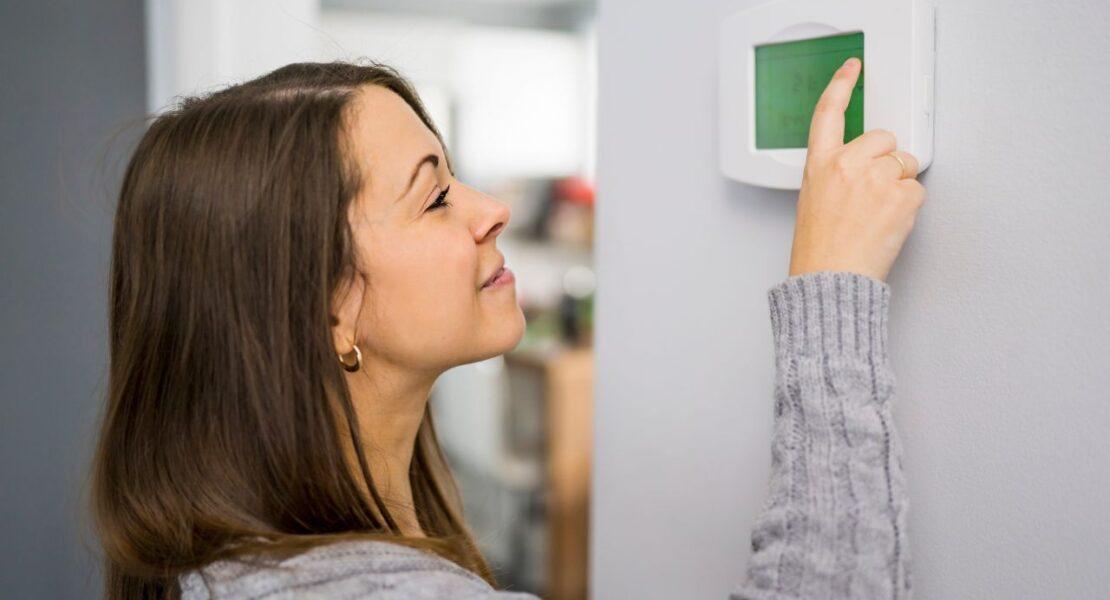 Woman adjusting a home thermostat to reduce heating and cooling costs.
