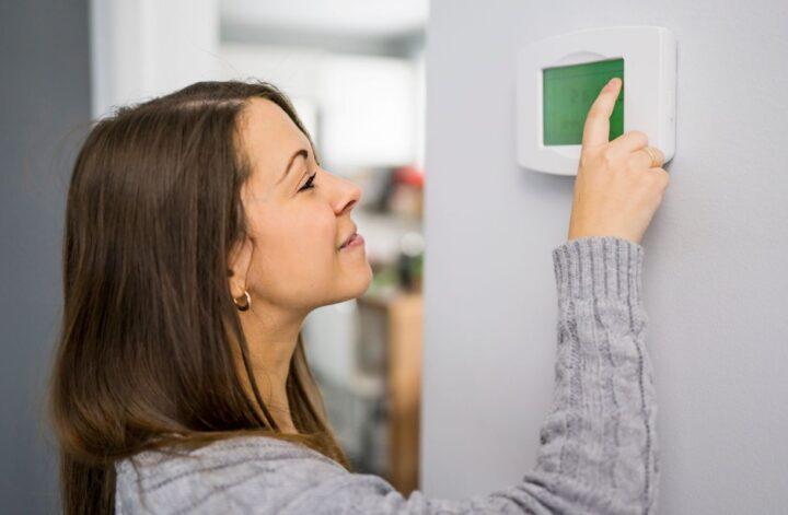 Woman adjusting a home thermostat to reduce heating and cooling costs.