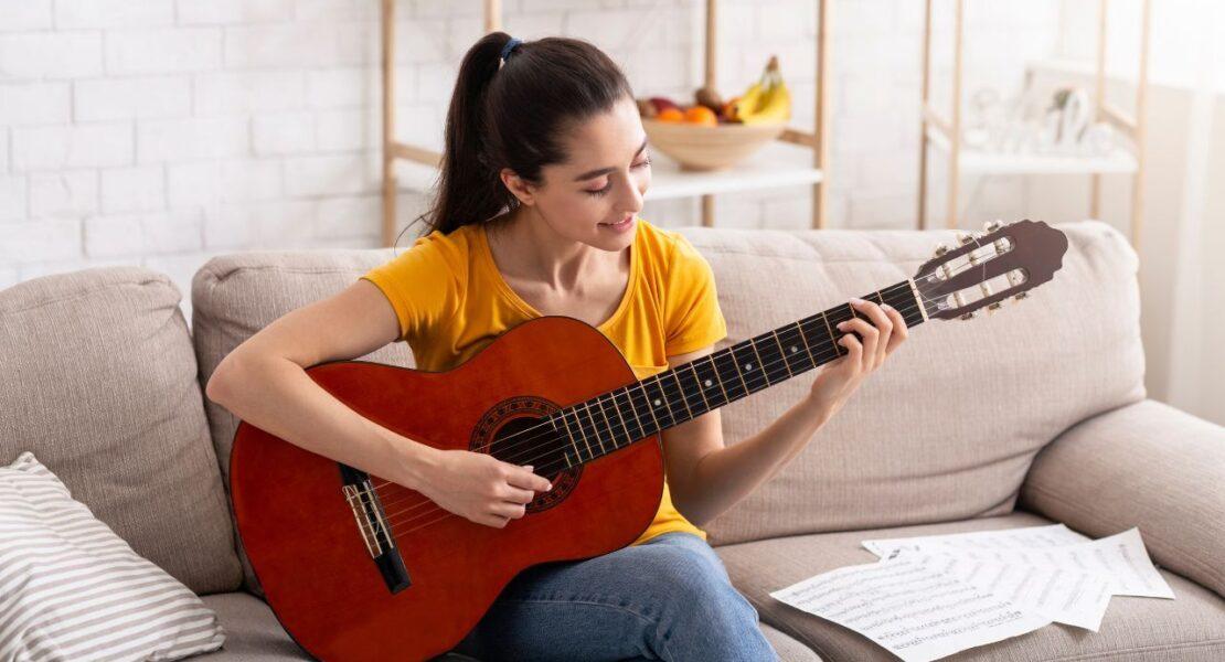 Young adult playing acoustic guitar at home as a screen-free hobby.